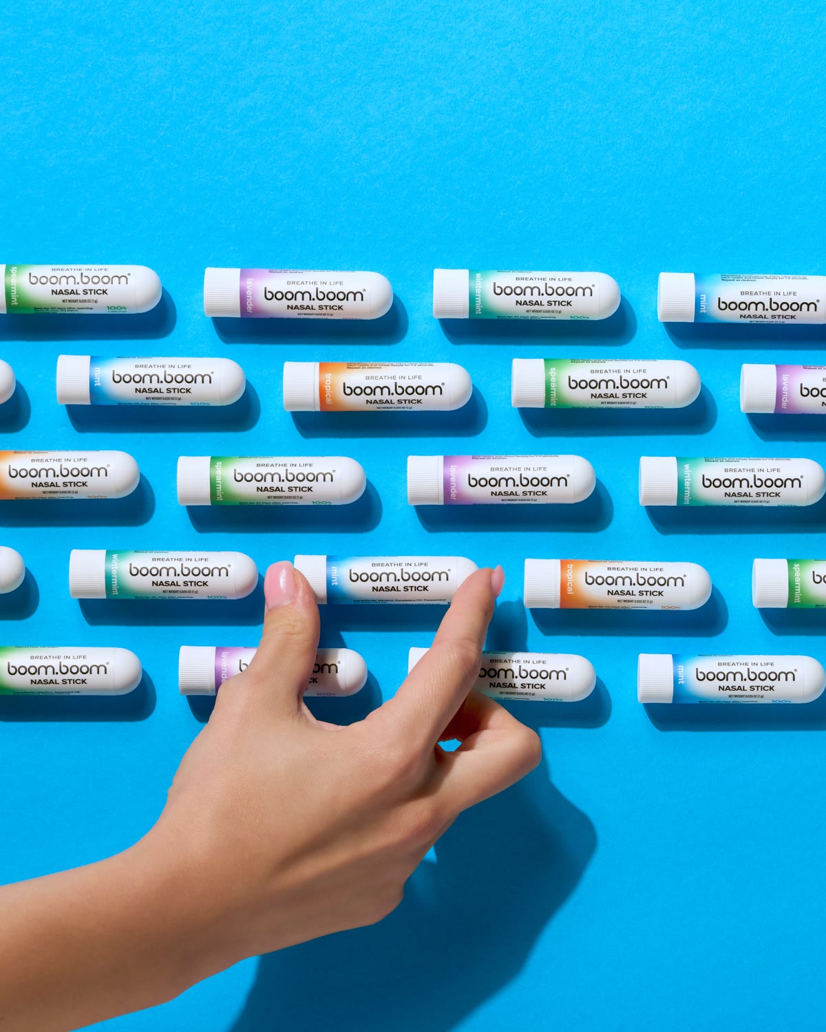 Rows of BoomBoom nasal sticks in every flavor, with a hand picking one