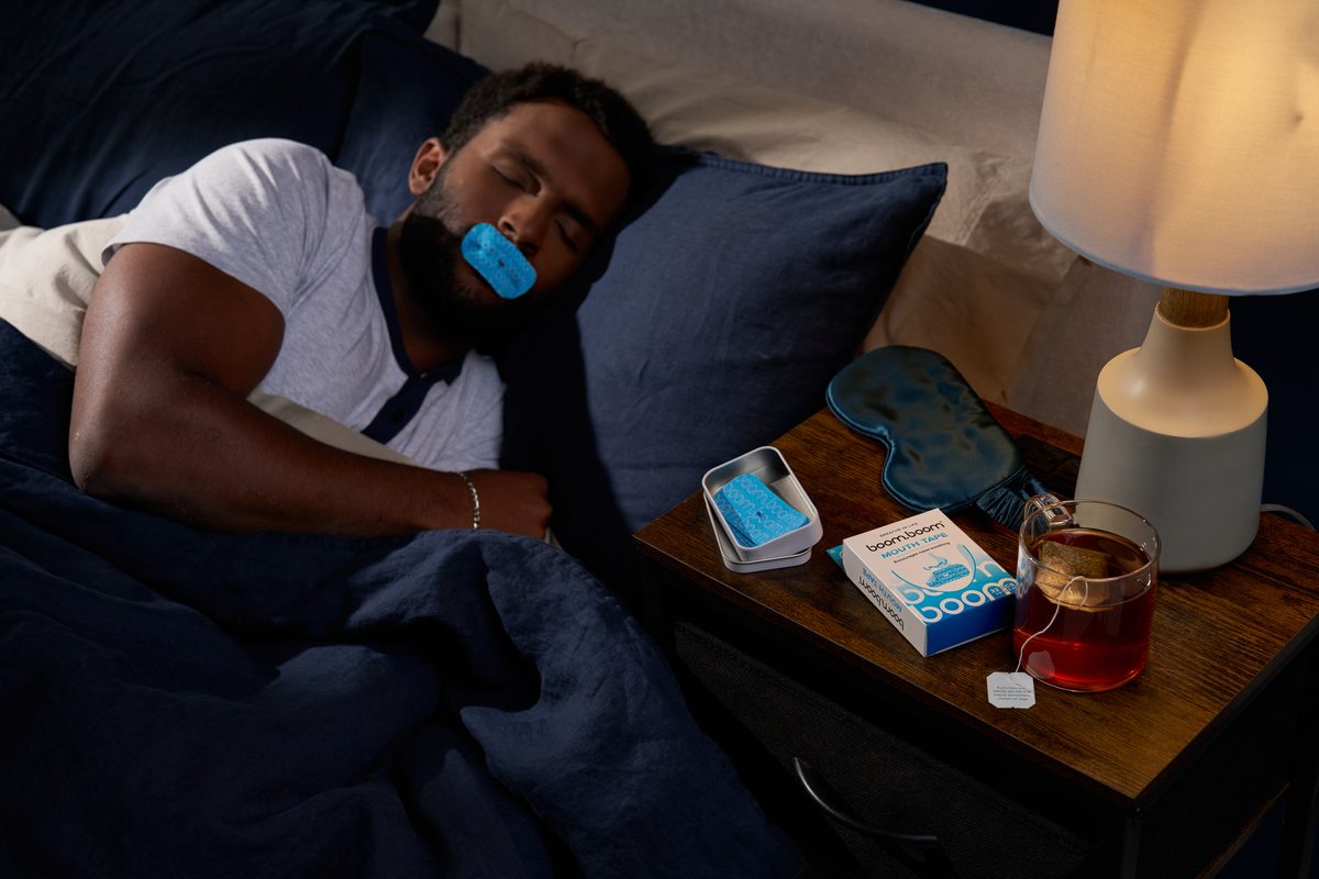 Man asleep wearing BoomBoom mouth tape, with the BoomBoom box on his nightstand